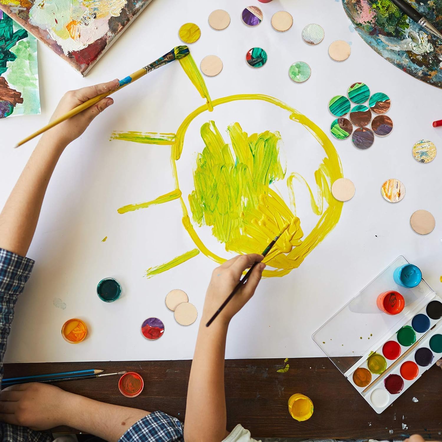 Child painting a yellow circle on a white sheet with watercolor paints and brushes.