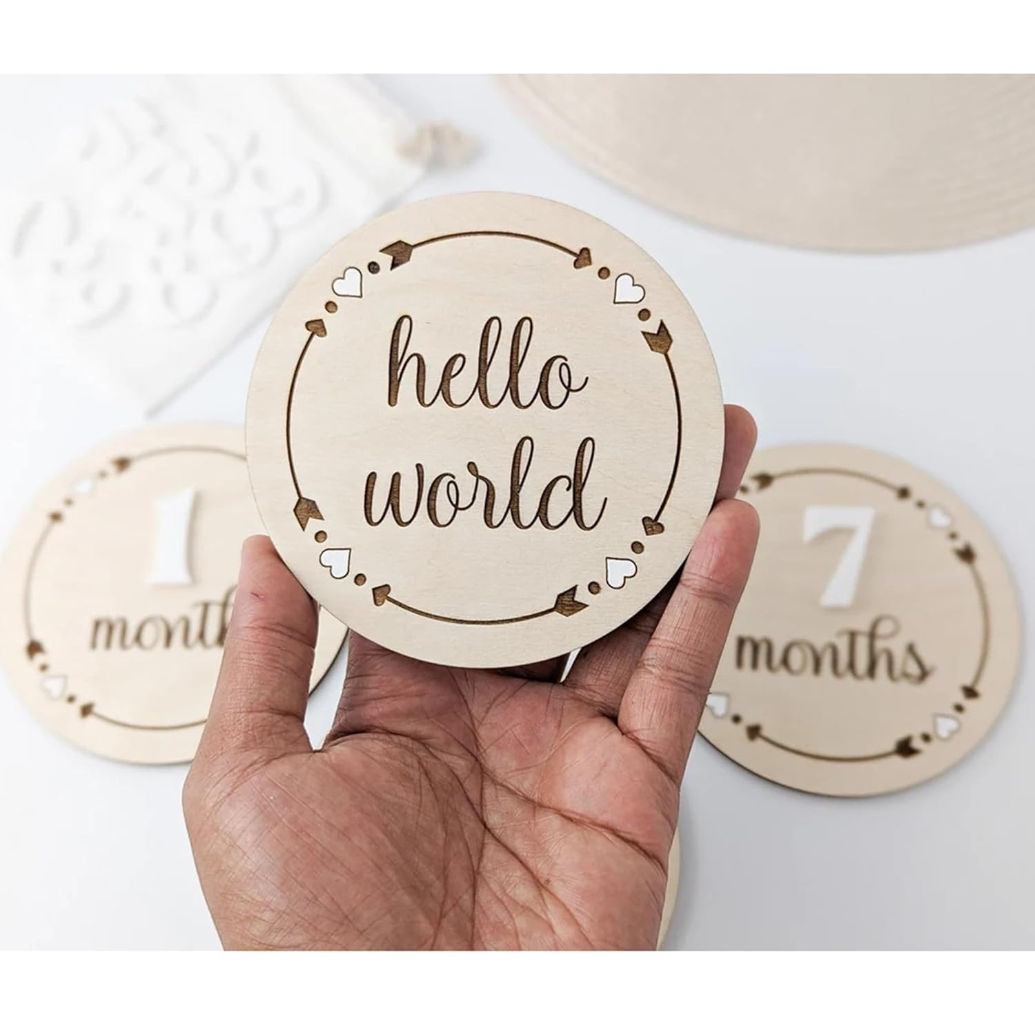 Hand holding a wooden disc with 'hello world' text, with other discs labeled '1 month' and '7 months' in the background.