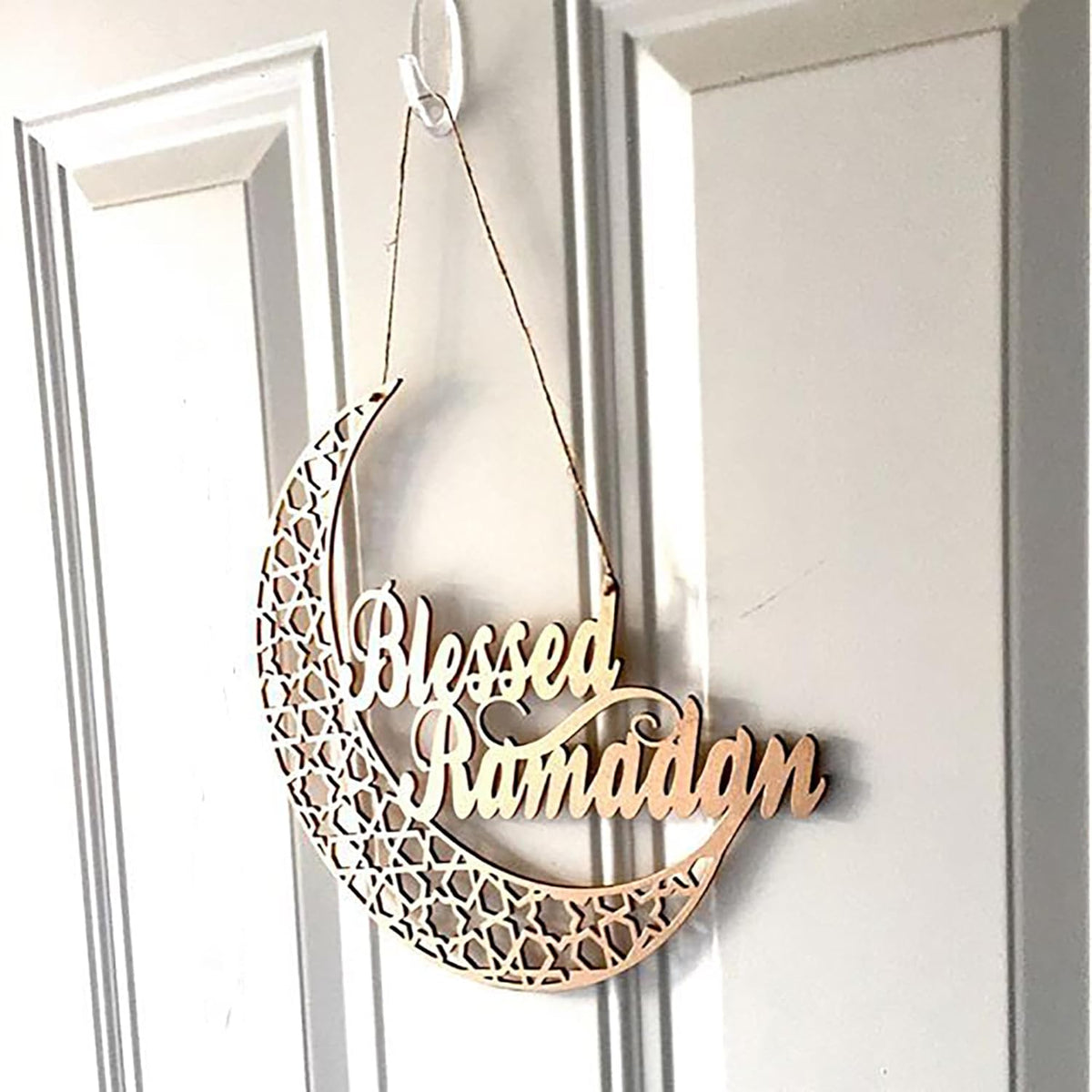 Decorative metal crescent moon with 'Blessed Ramadan' text hanging on a door.
