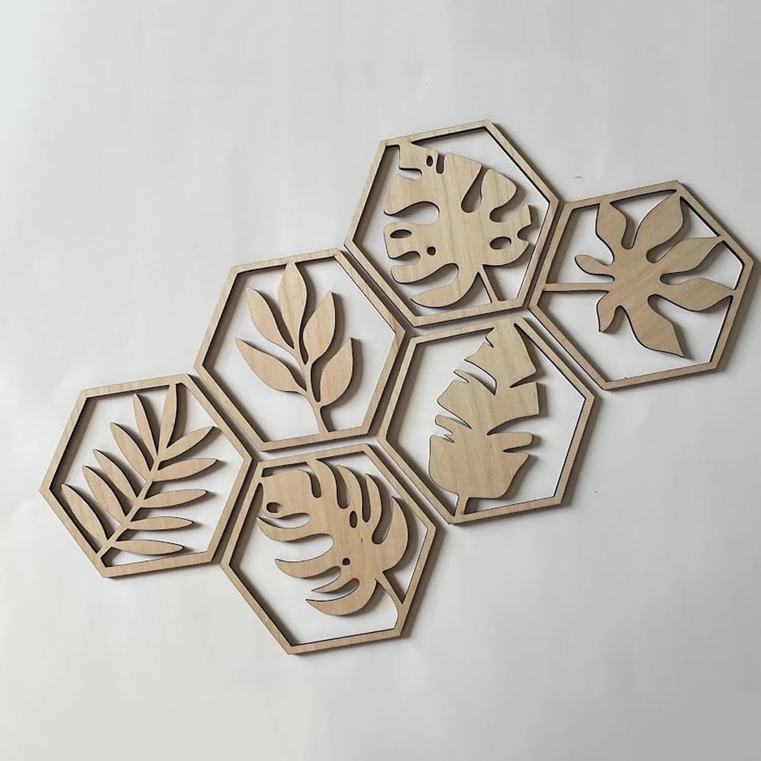 Hexagonal wooden wall art pieces with leaf patterns on a light gray background