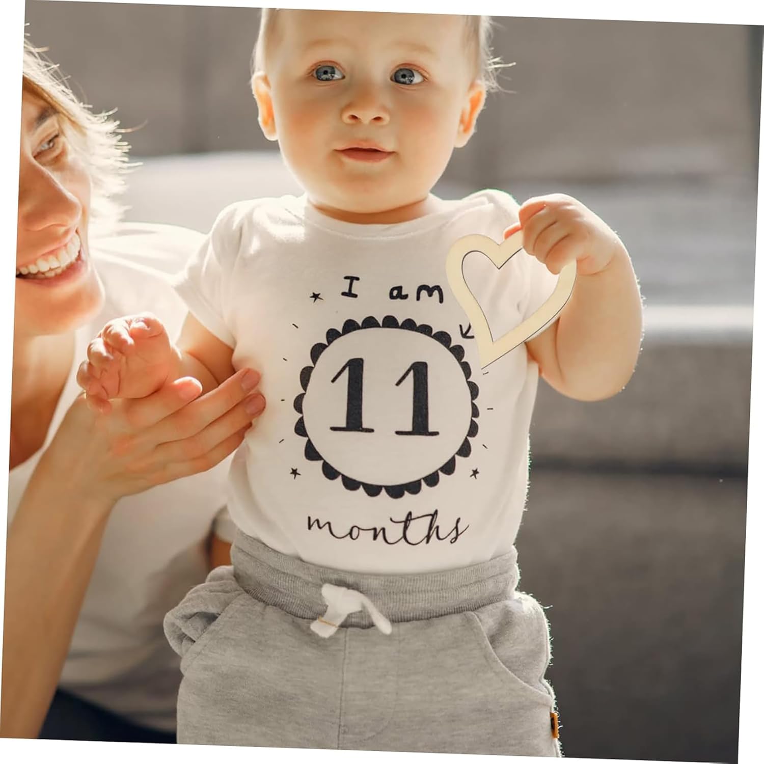Baby wearing a shirt with 'I am 11 months' text, held by a smiling woman.