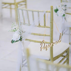 Gold 'Reserved' sign hanging on a chair with white flowers in an indoor setting