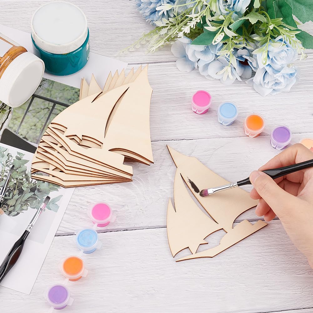 Person painting wooden sailboat cutouts on a table with paint containers and flowers.