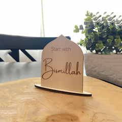 Wooden plaque with 'Start with Bismillah' text on a wooden surface with a blurred background