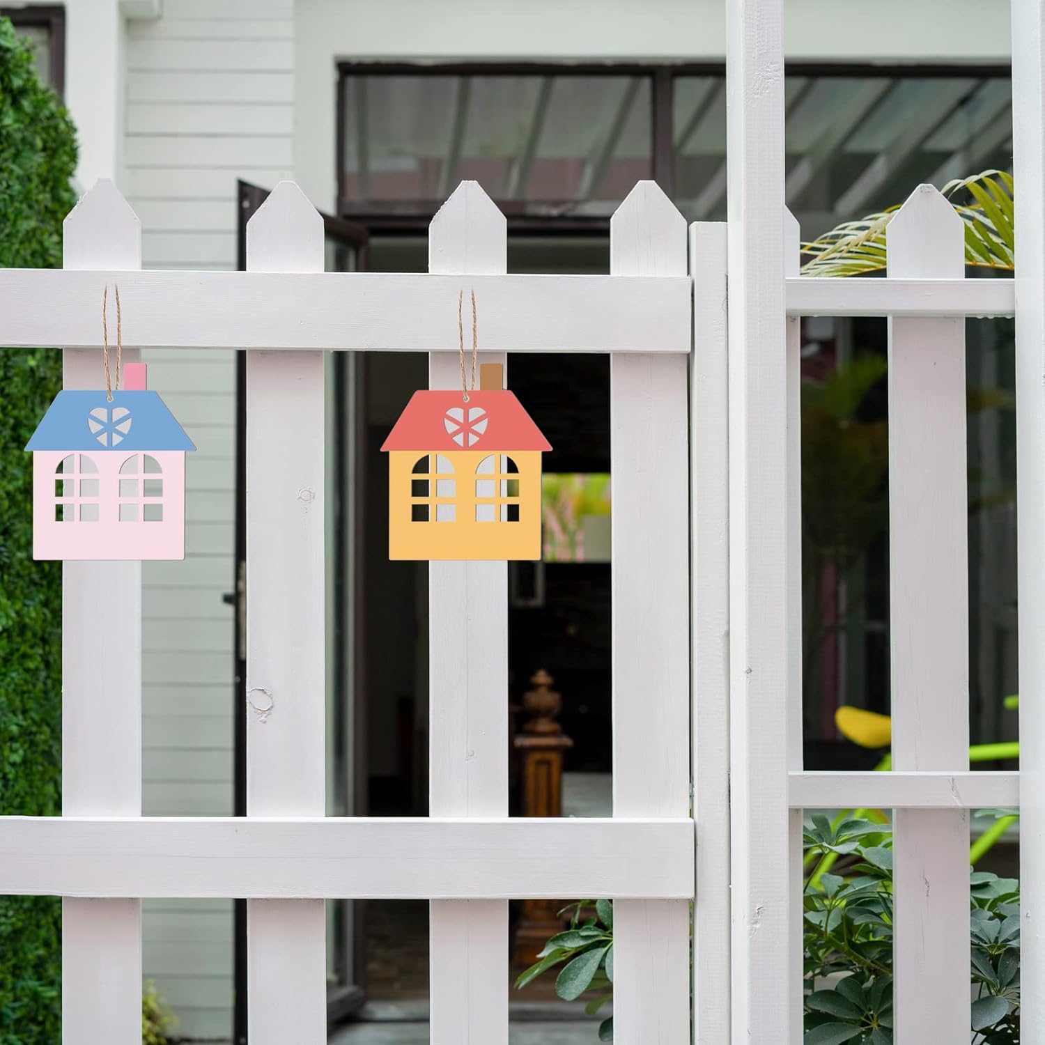 Colorful house-shaped decorations hanging on a white picket fence.