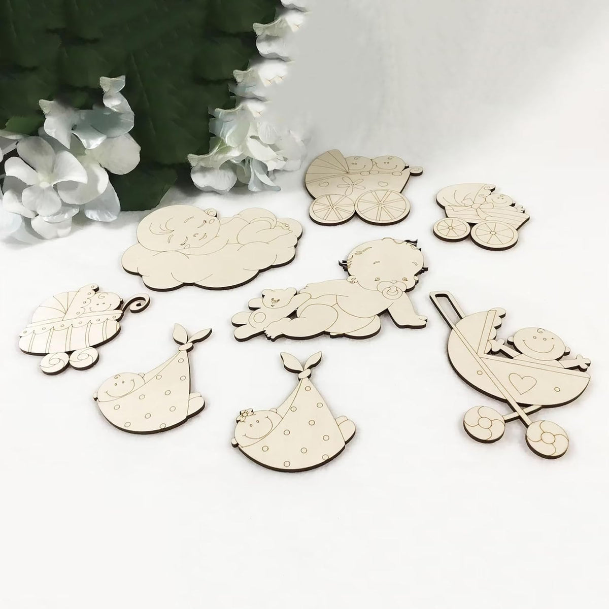 Set of wooden baby-themed decorations on a white surface with greenery in the background.