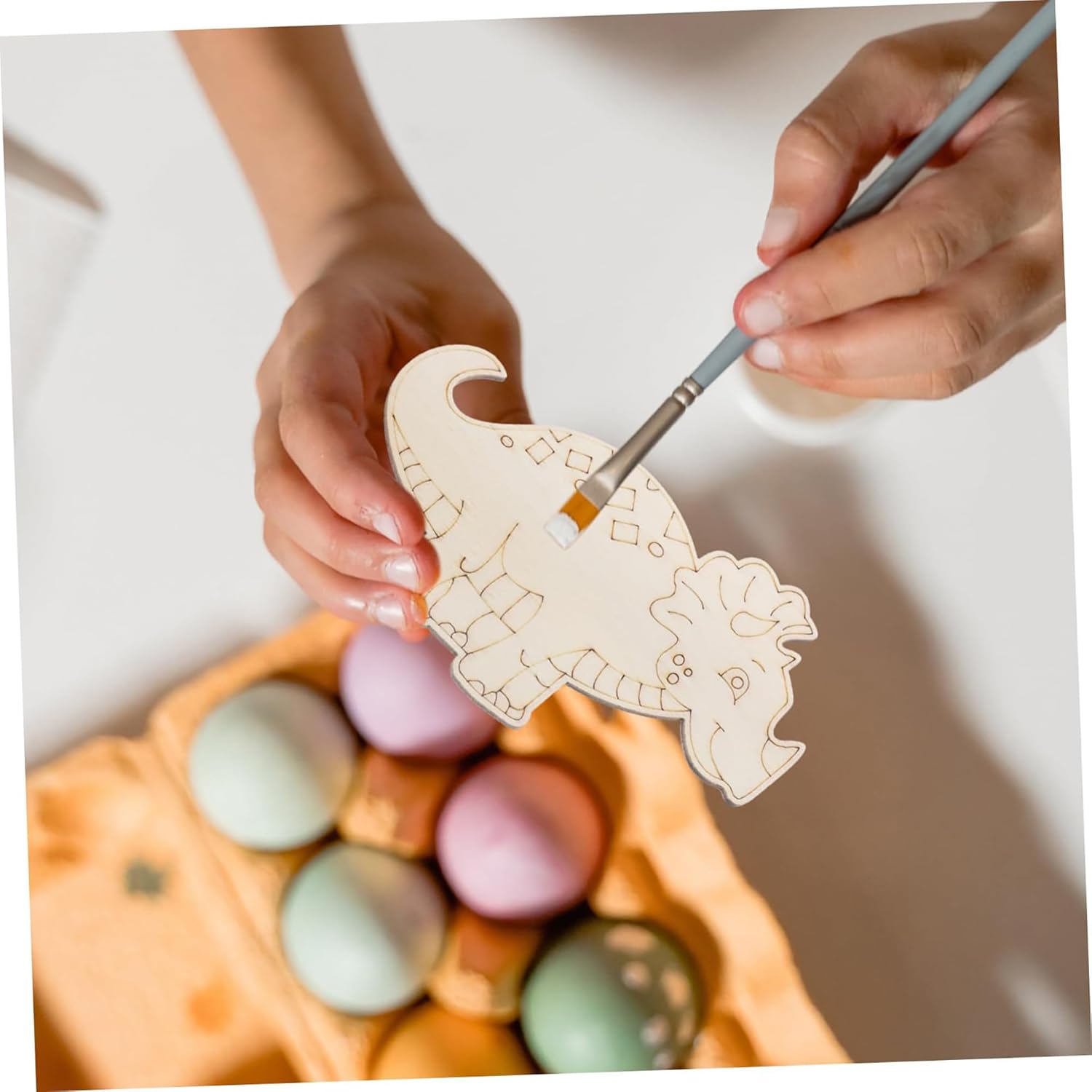 Person painting a wooden heart-shaped decoration with pastel Easter eggs in the background