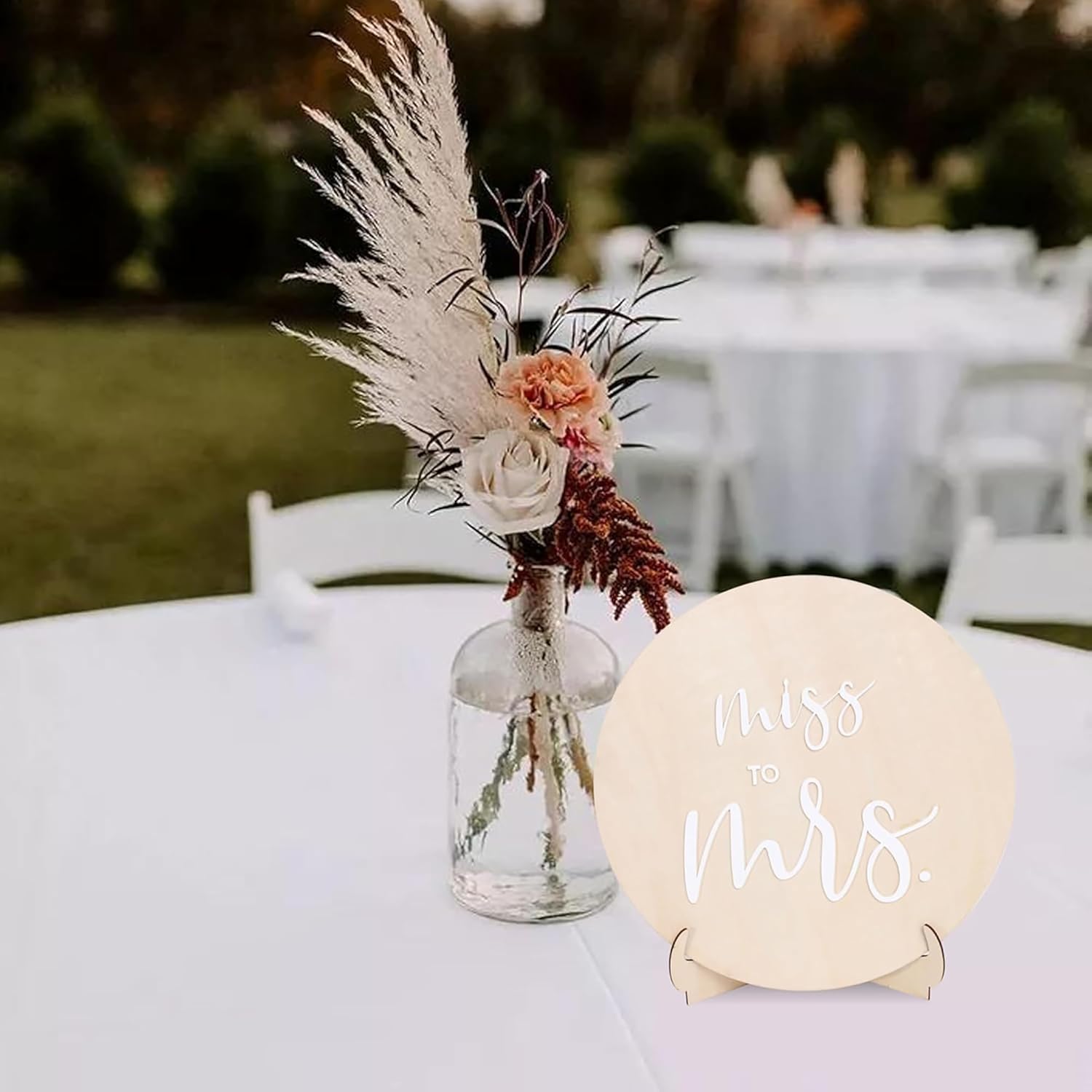 Decorative floral arrangement with pampas grass and flowers on a table, accompanied by a 'Miss to Mrs.' sign.