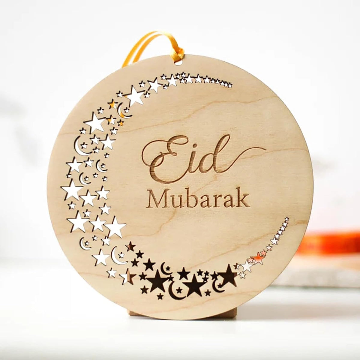 Wooden ornament with 'Eid Mubarak' text and star patterns on a white background
