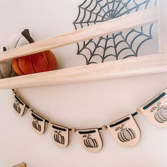 Halloween-themed decorative banner with pumpkins on a shelf with pumpkins and a spider web in the background.
