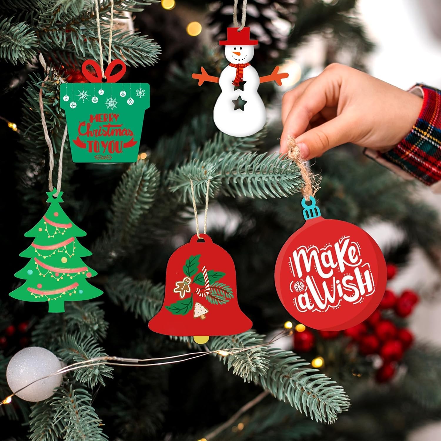 Hand hanging a red 'Make a Wish' ornament on a Christmas tree with other decorations.