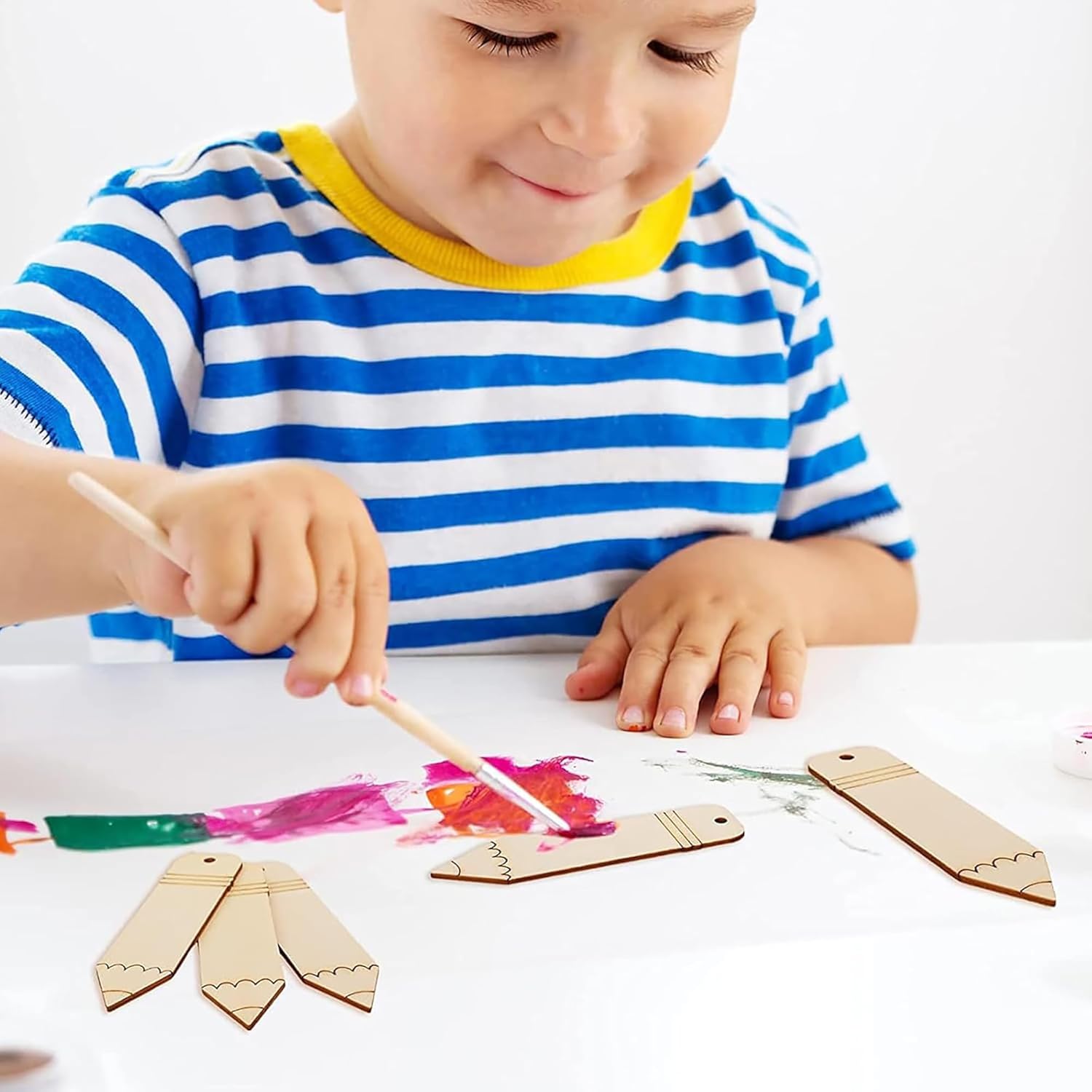 Child painting wooden tags with colorful paint on a white surface