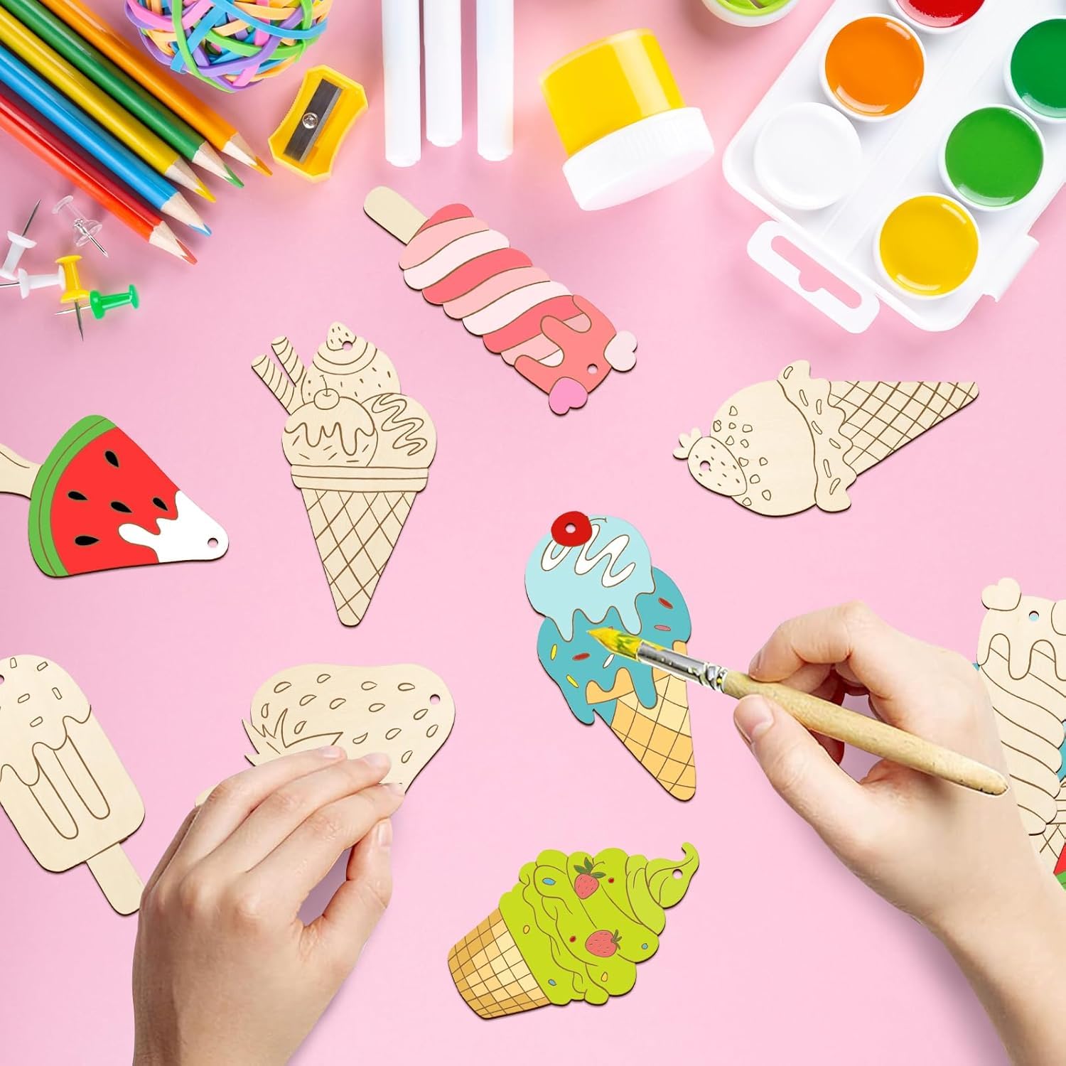 Colorful craft materials including ice cream cones, watermelon slices, and paintbrushes on a pink background.