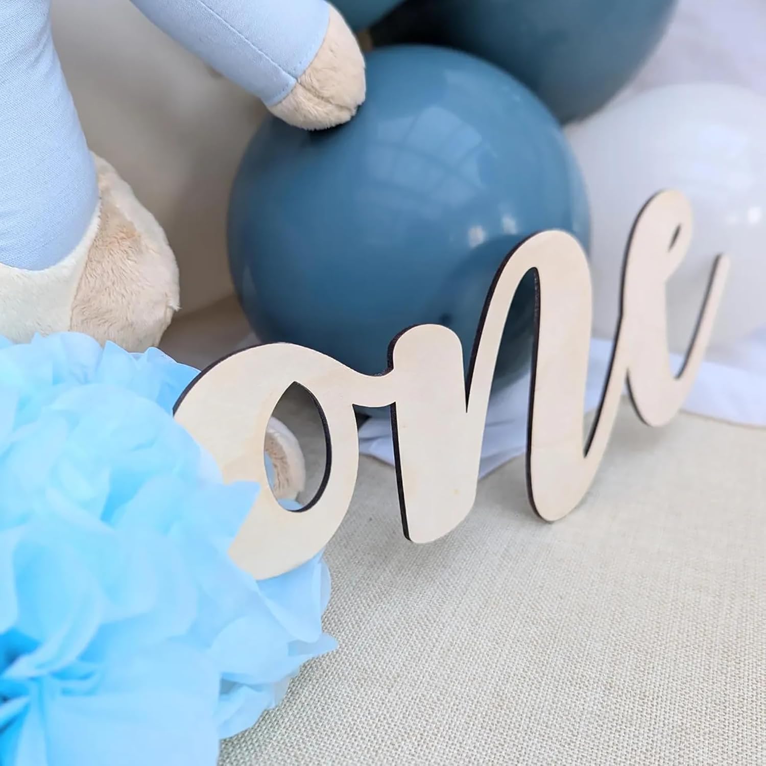 Wooden number 'one' with balloons and pom-poms in blue and white on a neutral background