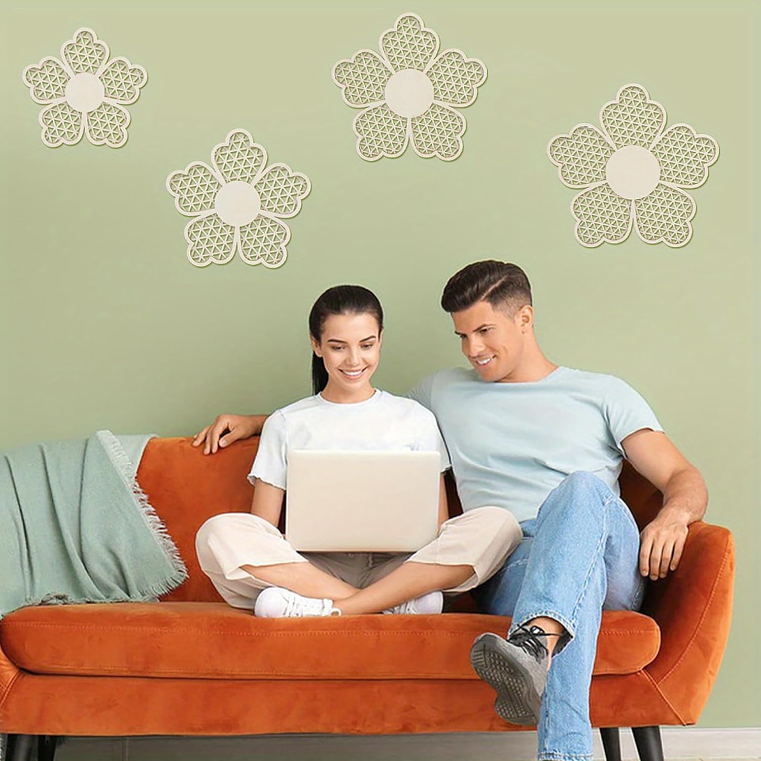Two people sitting on an orange couch with a laptop, against a light green wall with decorative flower patterns.