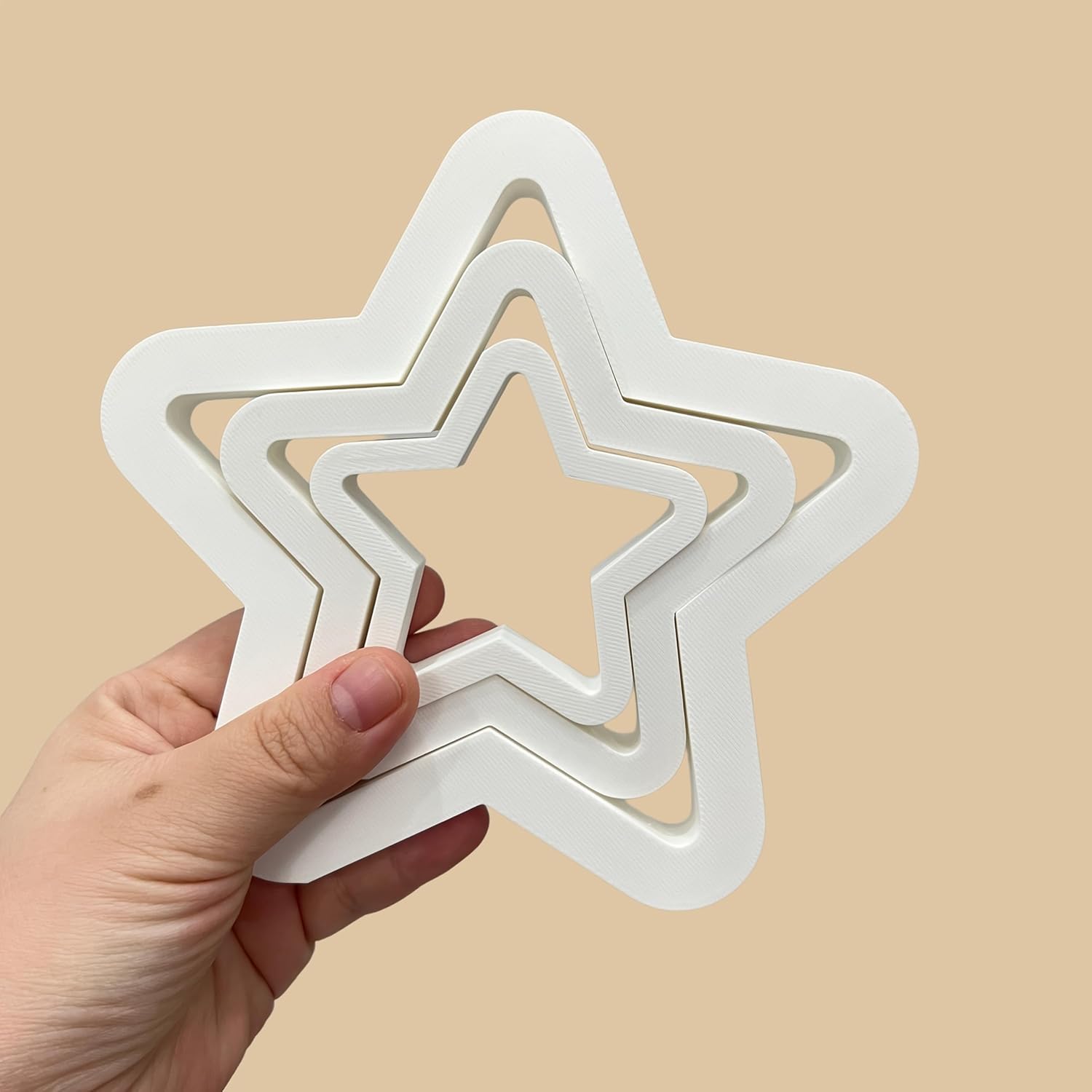 Hand holding a set of white star-shaped cookie cutters against a beige background