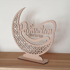 Decorative wooden crescent moon with 'Ramadan mubarak' text on a wooden surface.