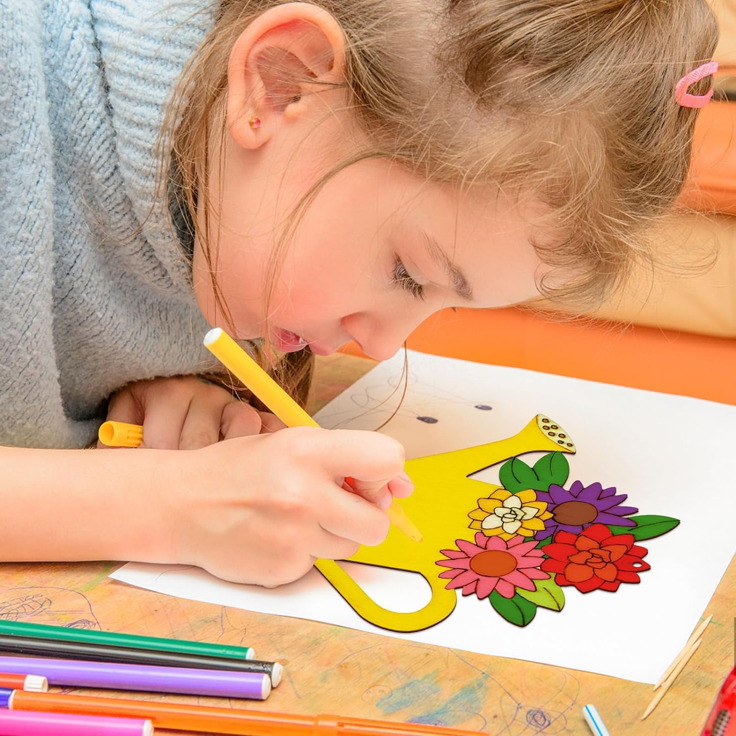 Child coloring a flower design with markers on a table.