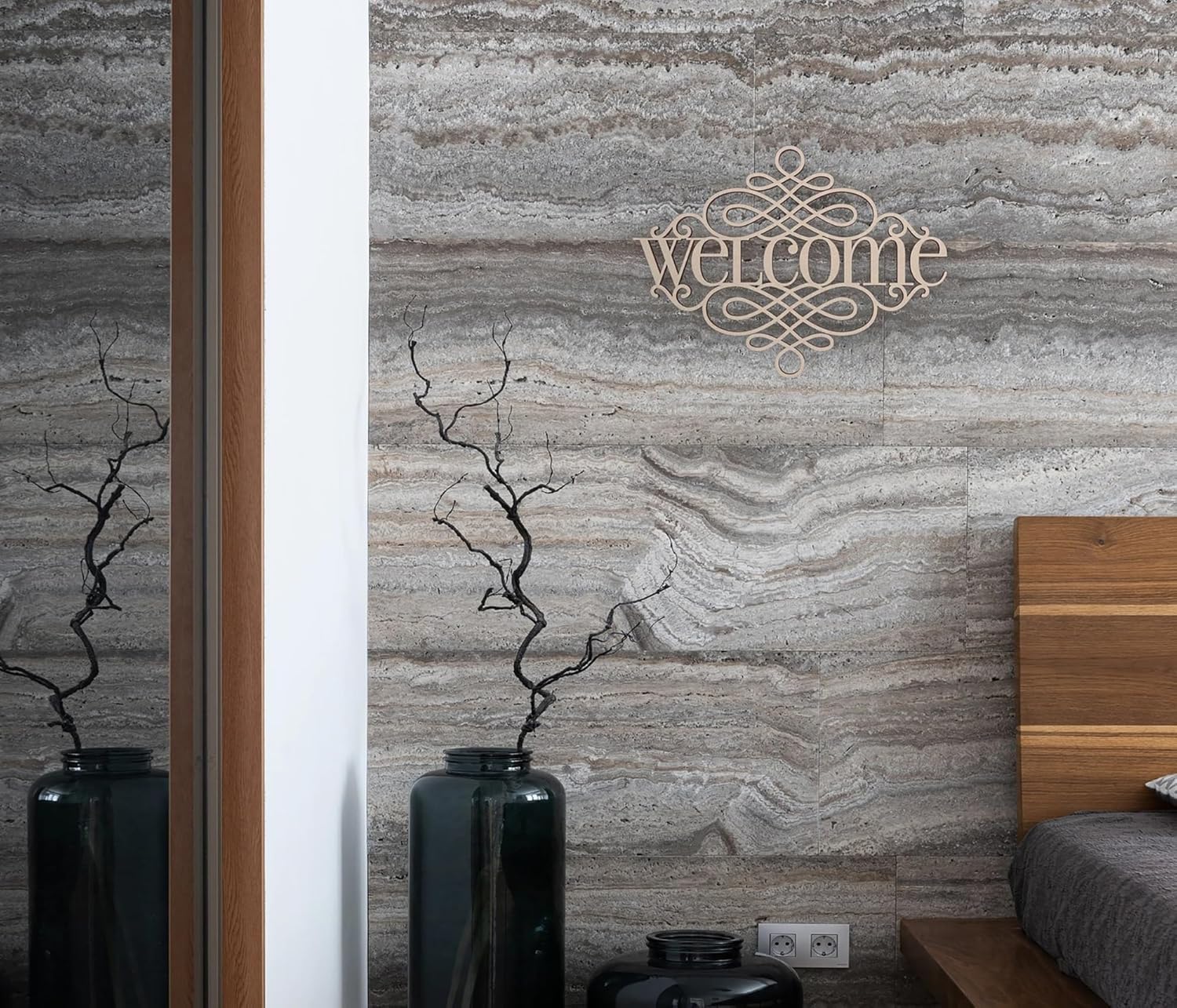 Decorative wall art with 'Welcome' on a stone-patterned wall, flanked by vases and a bed.