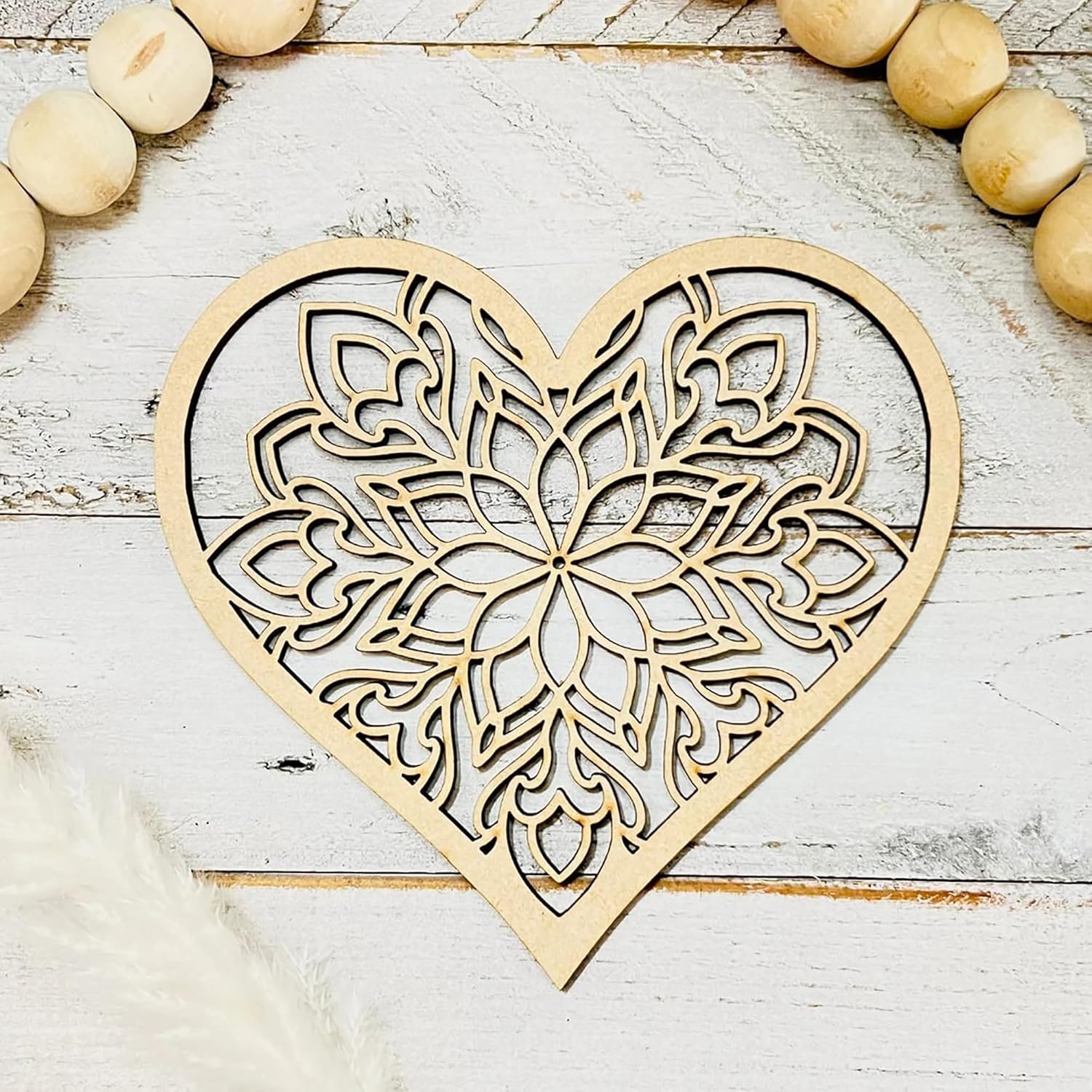 Wooden heart-shaped decorative item with intricate cut-out patterns on a light wooden surface.
