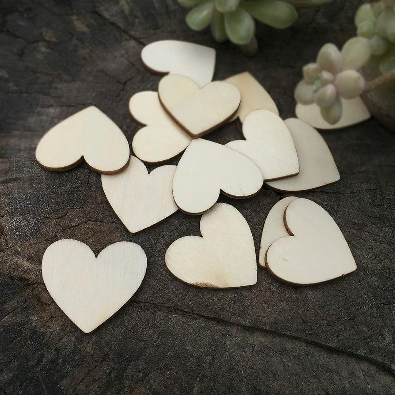 Wooden heart shapes on a dark surface with succulents in the background