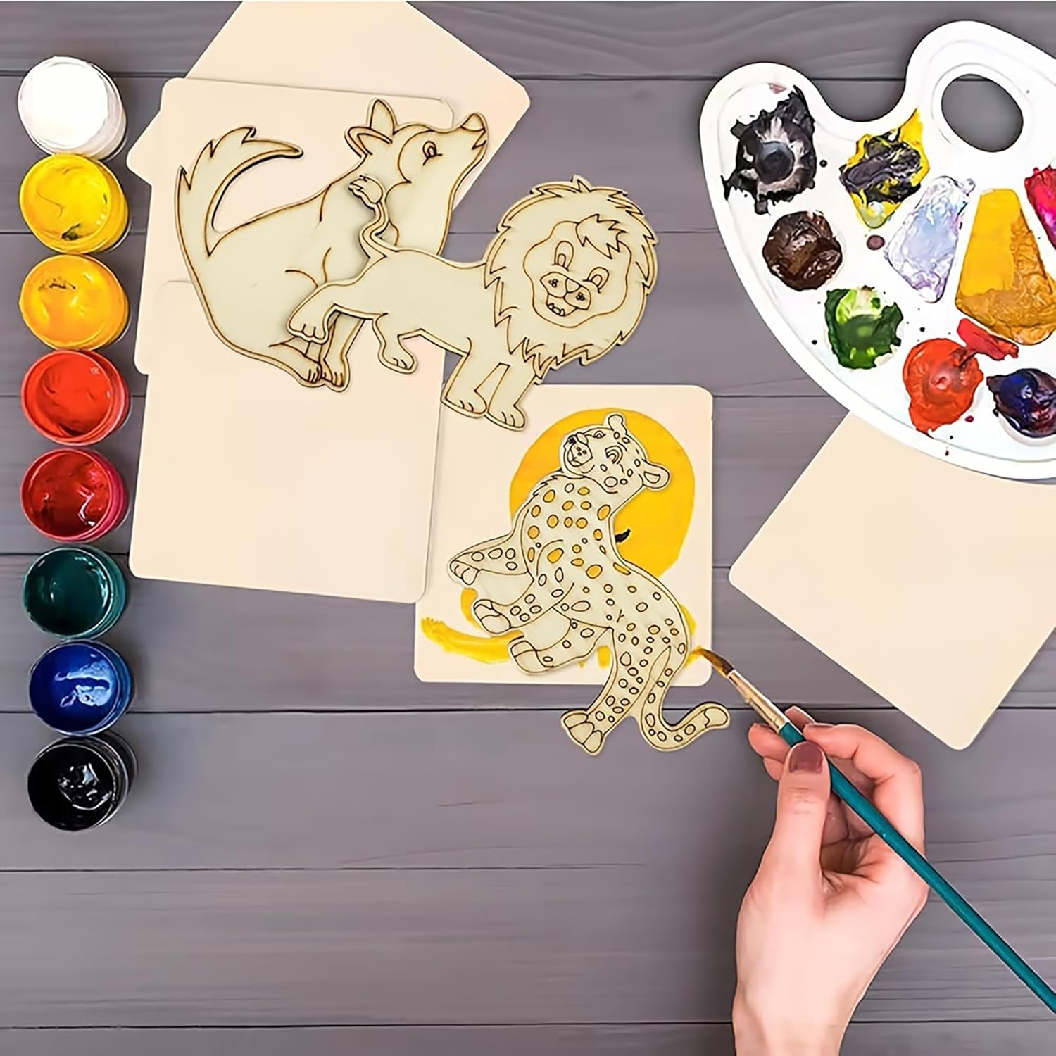 Wooden animal shapes with paint and a hand painting one of them on a wooden surface.