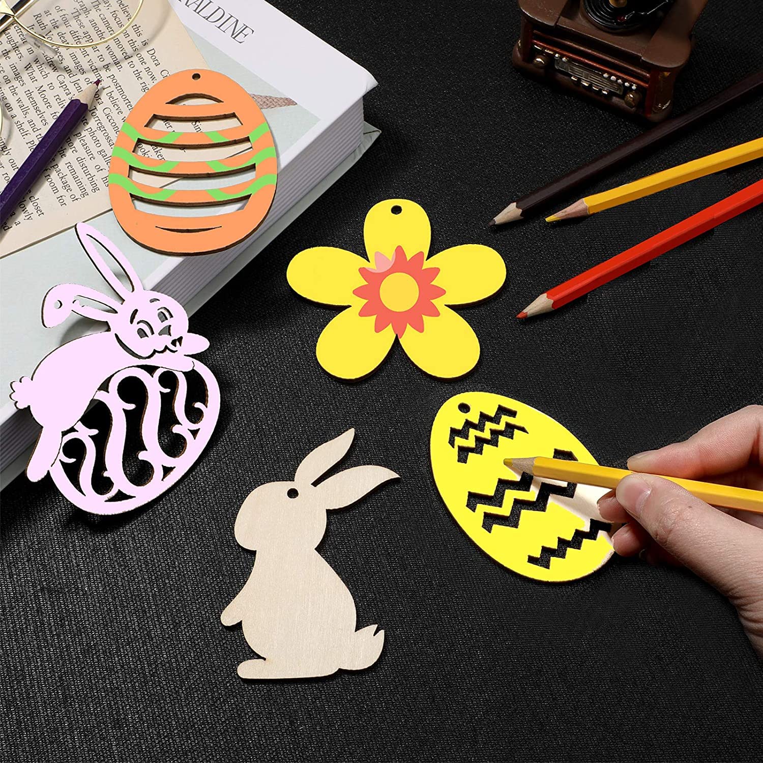Colorful paper cutouts of Easter-themed shapes on a black surface with pencils.