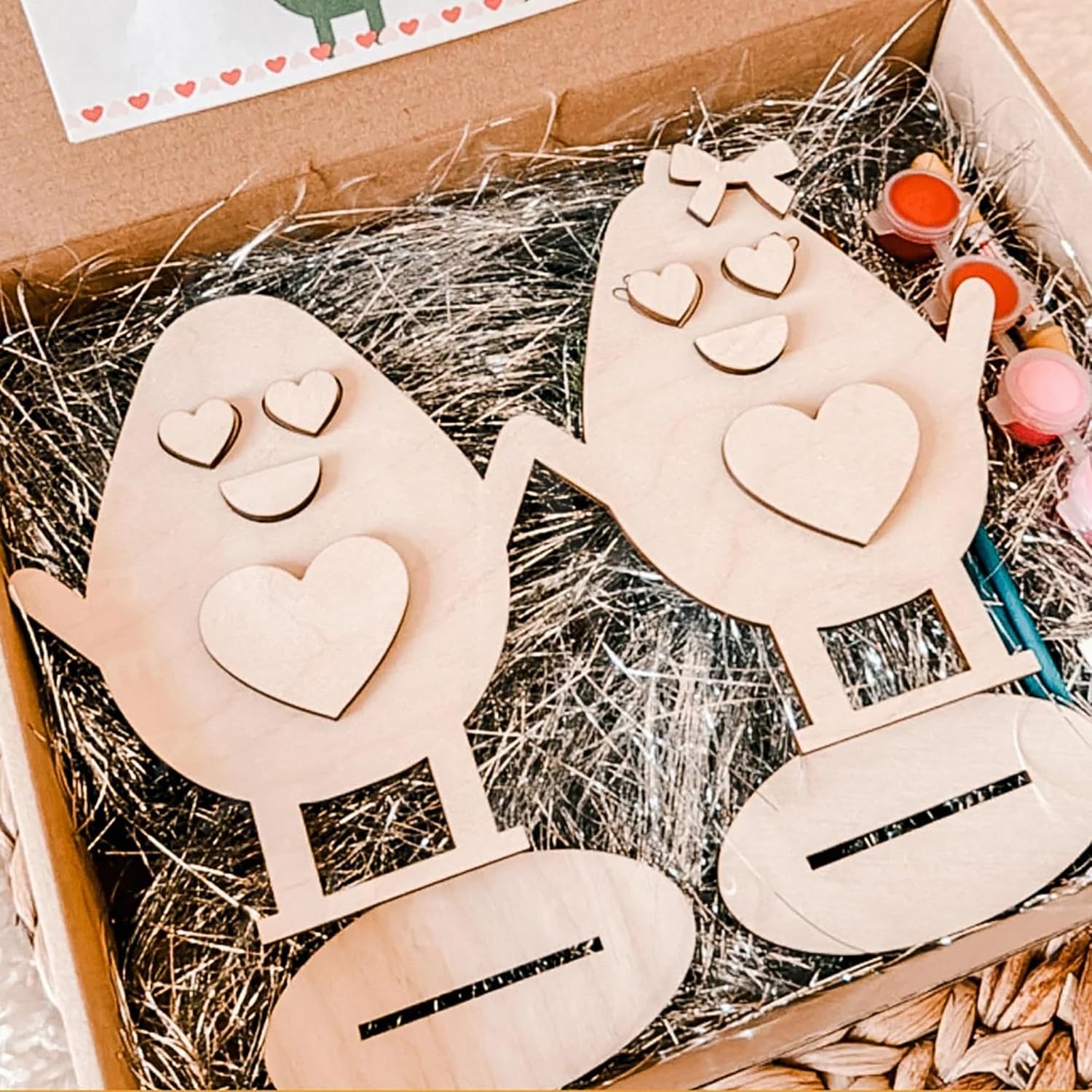 Wooden house-shaped cutouts with heart details on a straw-lined box.