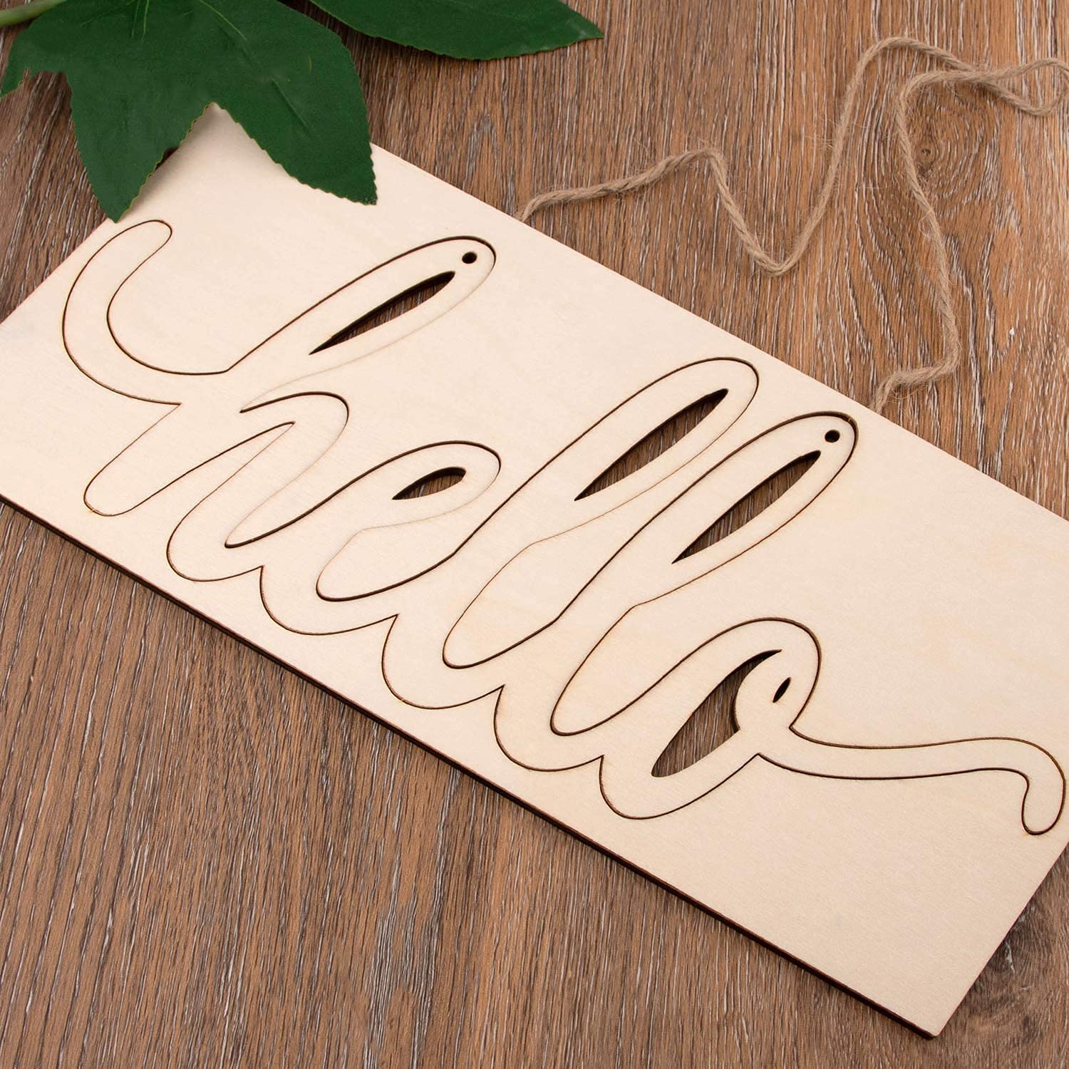 Wooden cutout letters spelling 'Hello' on a wooden surface with leaves and twine.