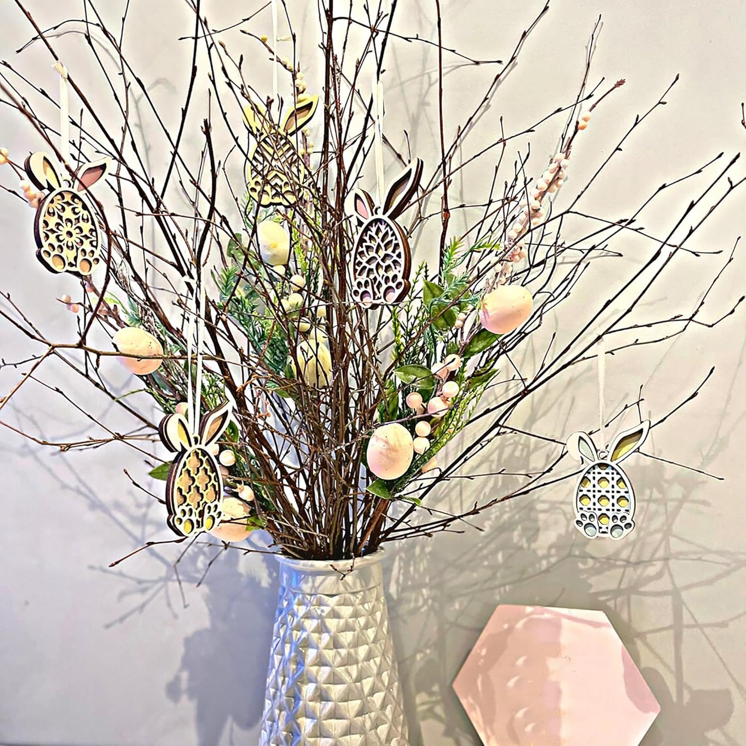 Decorative arrangement with branches, Easter eggs, and bunny ornaments in a vase on a light background.