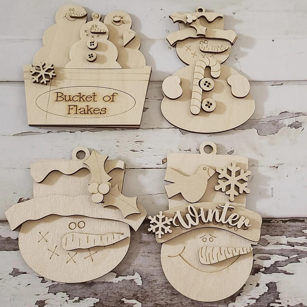 Wooden Christmas ornaments shaped like a bucket of snowflakes, snowman, and other winter-themed items on a rustic wooden background.
