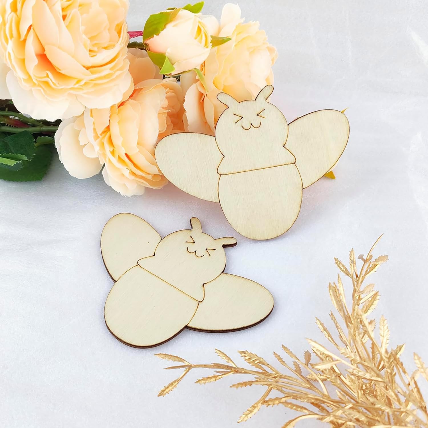 Two wooden butterfly decorations on a white surface with flowers and gold leaves.