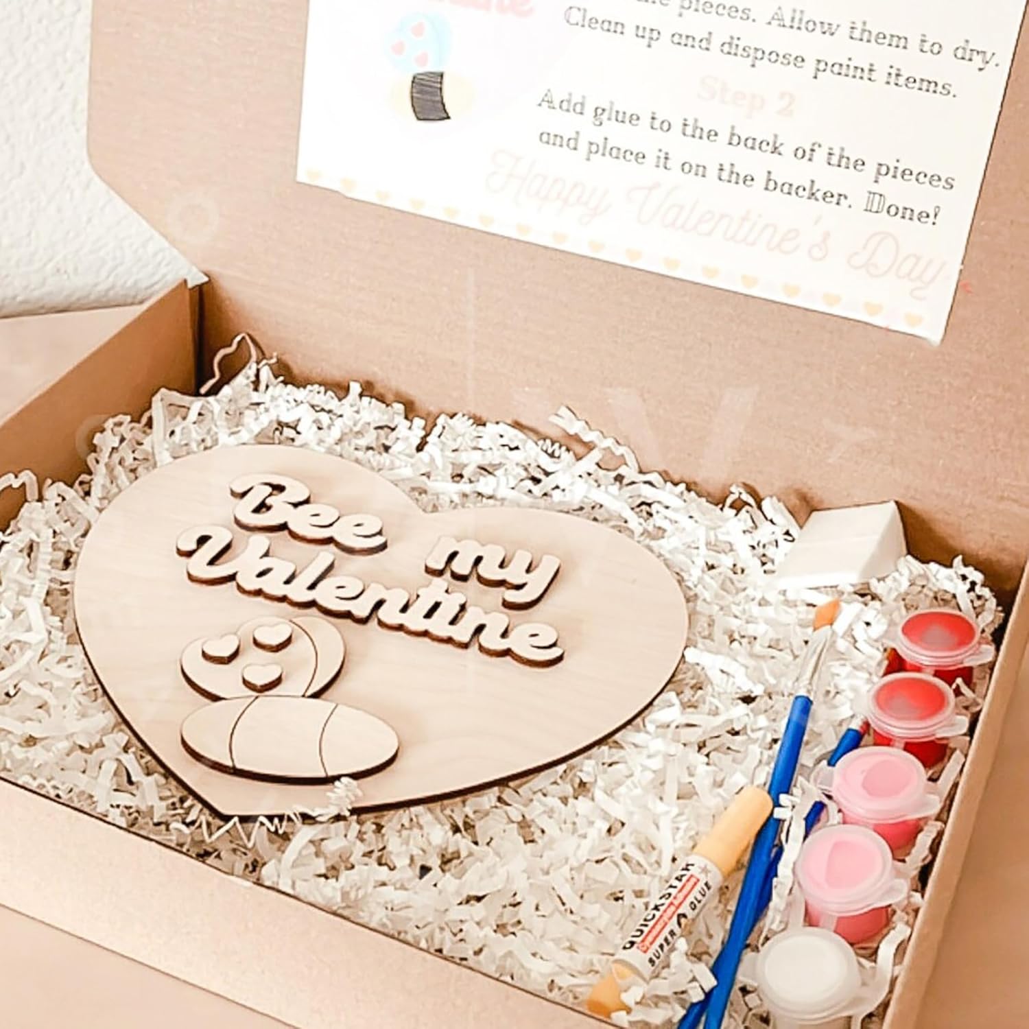 Wooden heart-shaped plaque with 'Bee my Valentine' text, paint supplies, and instructions in a box.