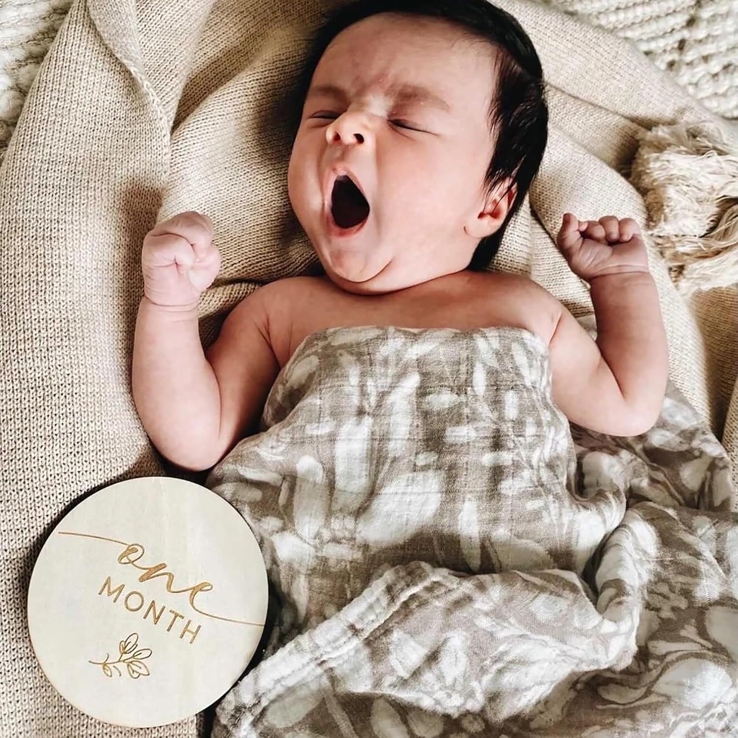 Newborn baby yawning with a 'one month' milestone disc in the foreground
