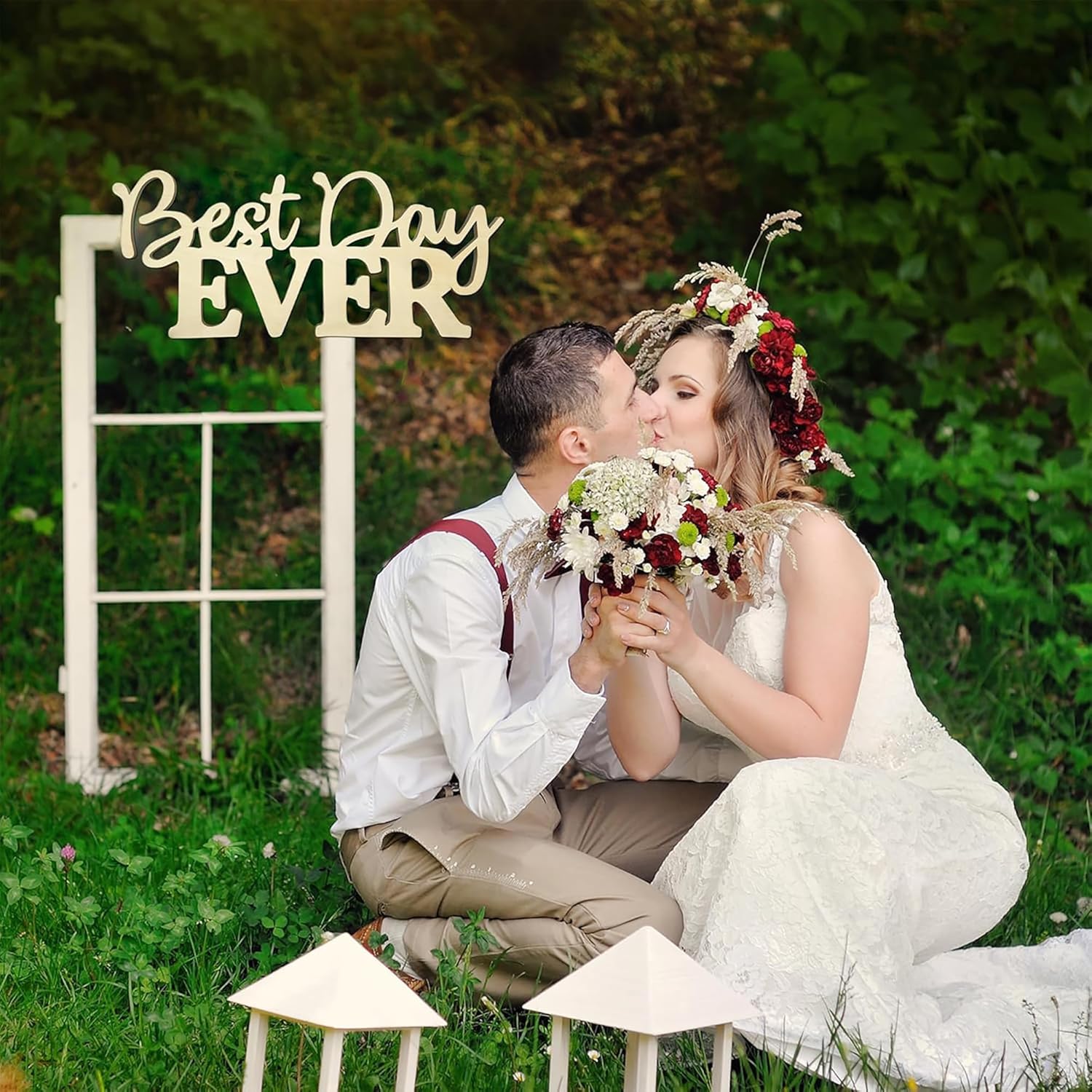 Couple in wedding attire with 'Best Day Ever' sign in a natural setting