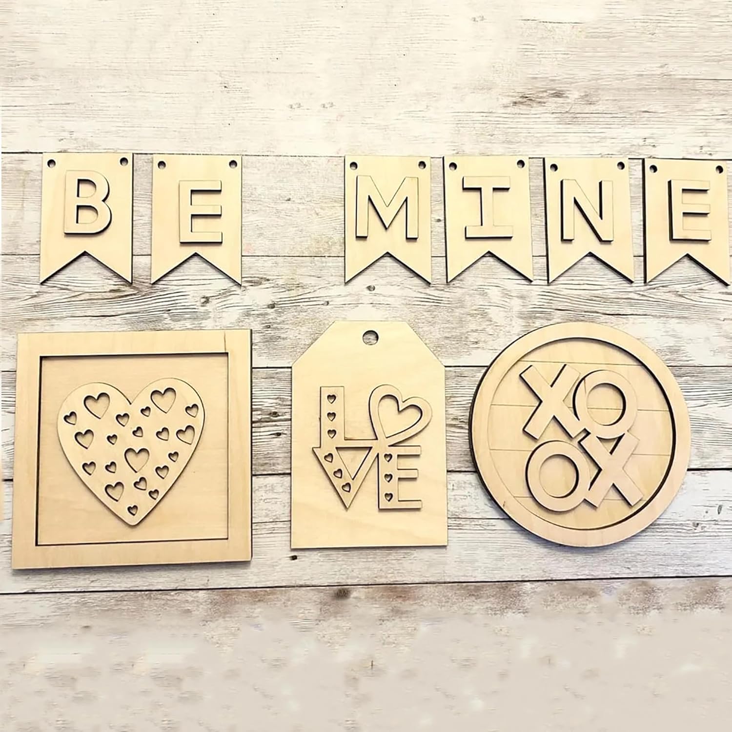 Wooden decorations with 'BE MINE' banner, heart designs, and 'XO & K' on a wooden surface.