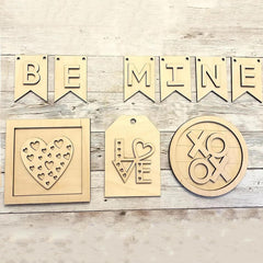 Wooden decorations with 'BE MINE' banner, heart designs, and 'XO & K' on a wooden surface.