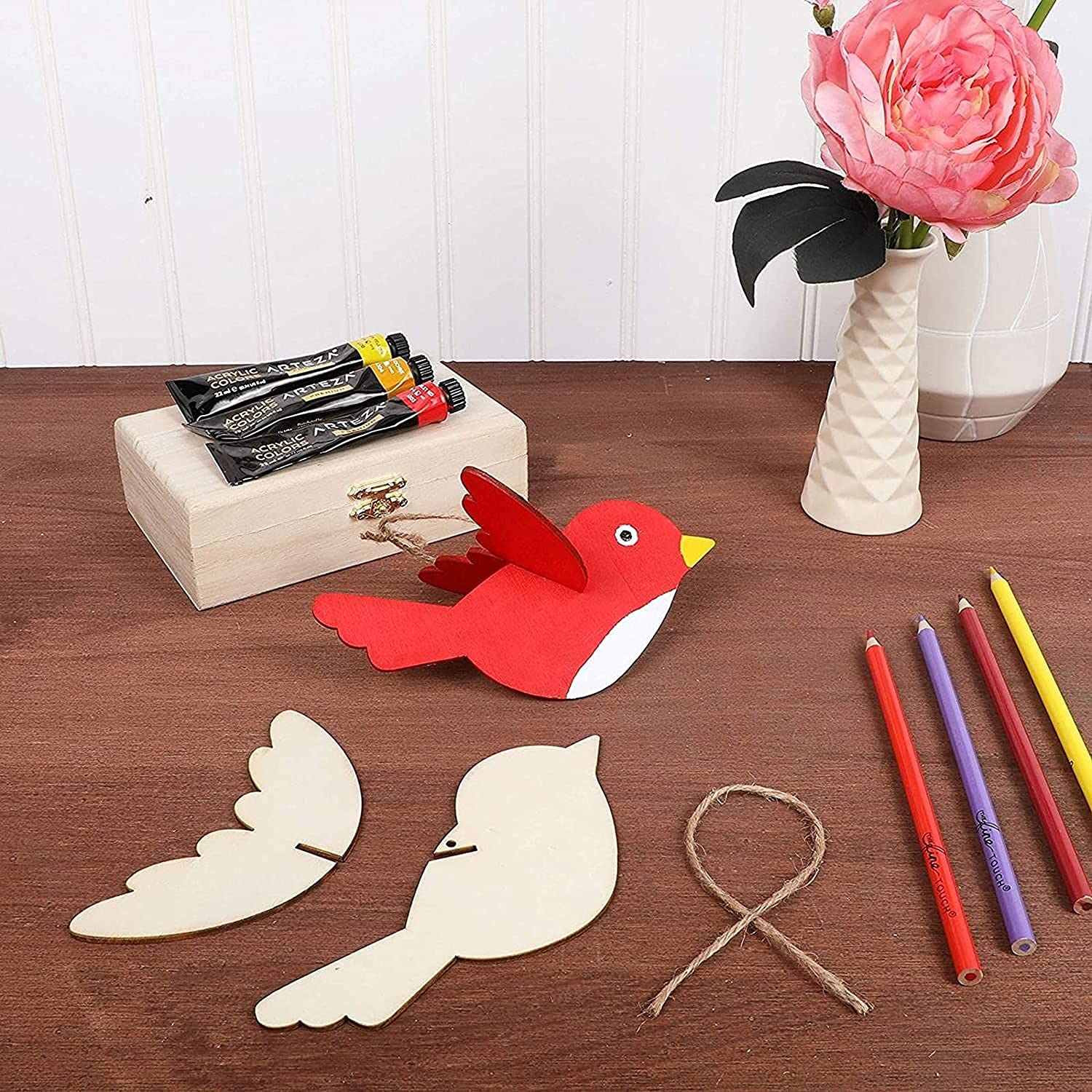 Red bird craft kit with wooden pieces, string, and markers on a wooden surface.