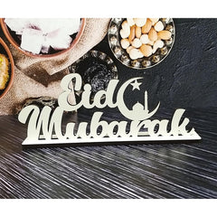 Decorative sign with 'Oid Mubarak' on a dark surface with food items.