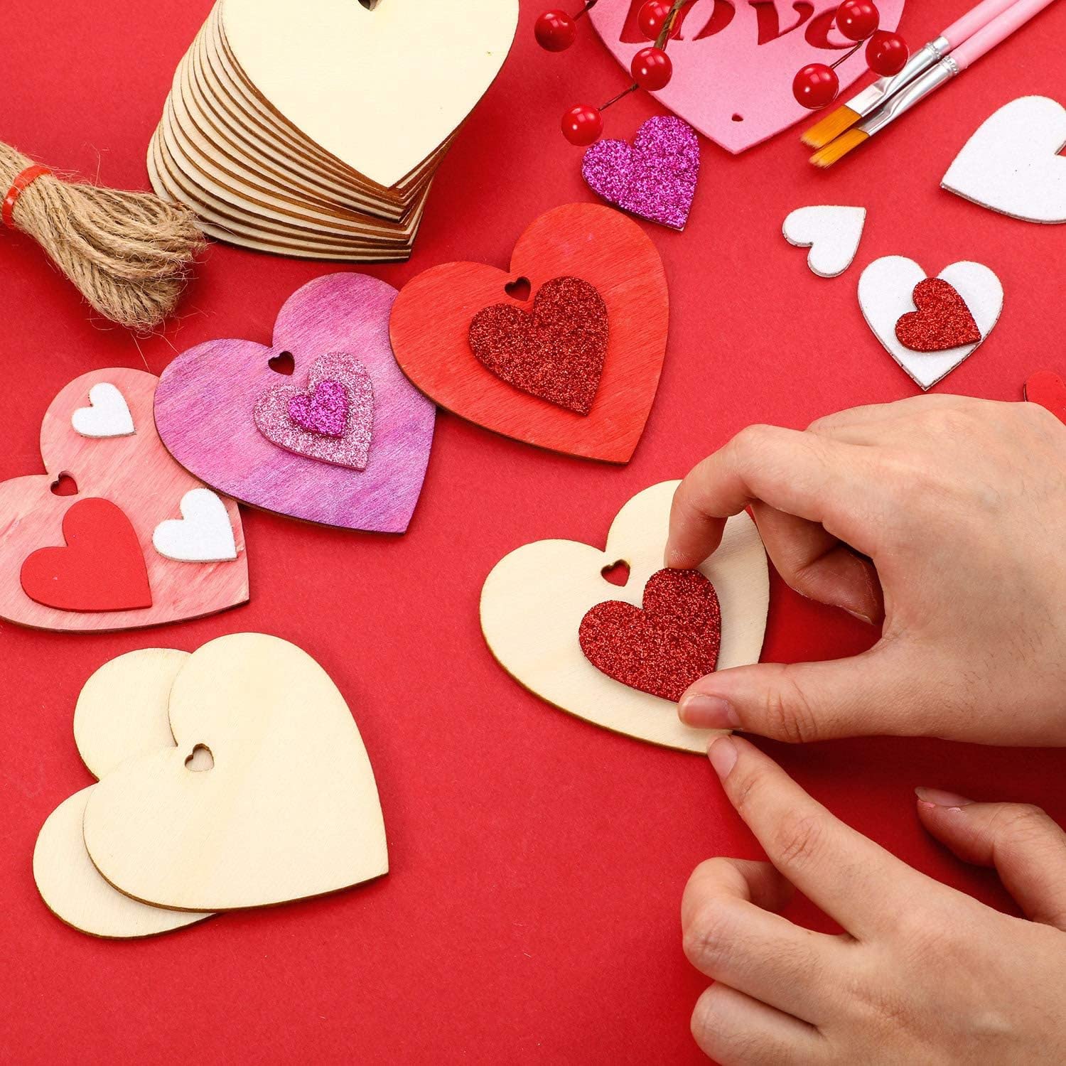 Heart-shaped paper crafts on a red background with hands arranging them.