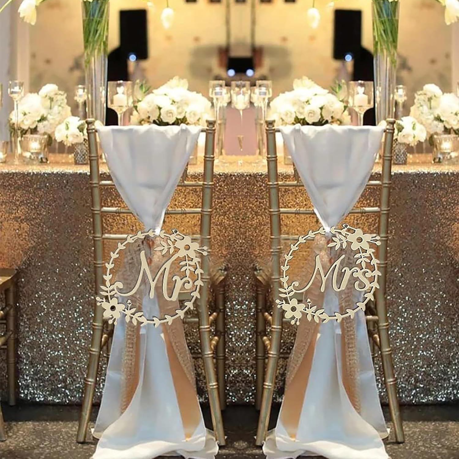 Decorative chair covers with 'Mr' and 'Mrs' signs on a table with floral arrangements.