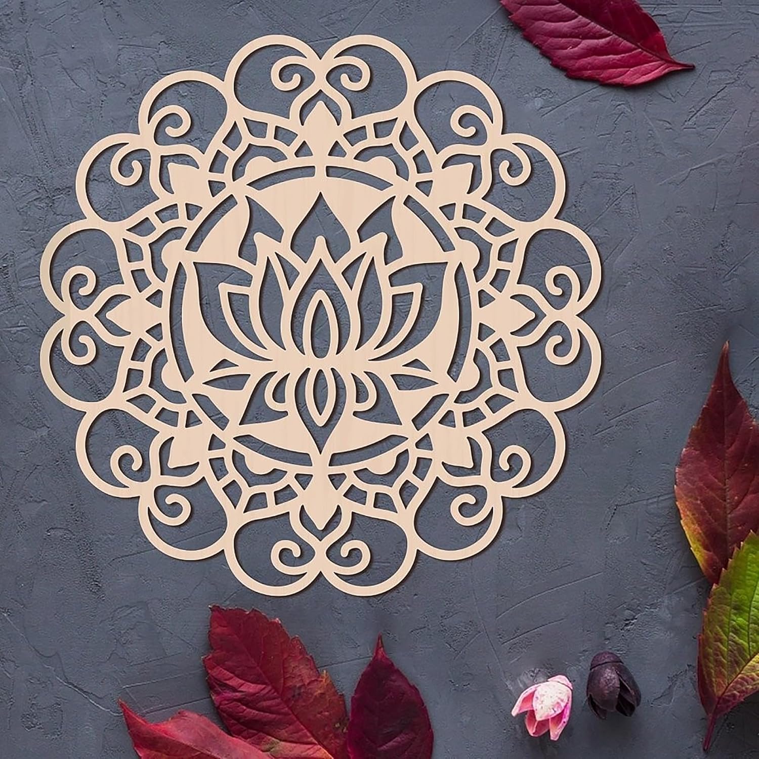 Decorative wooden mandala with intricate patterns on a dark surface with red leaves.