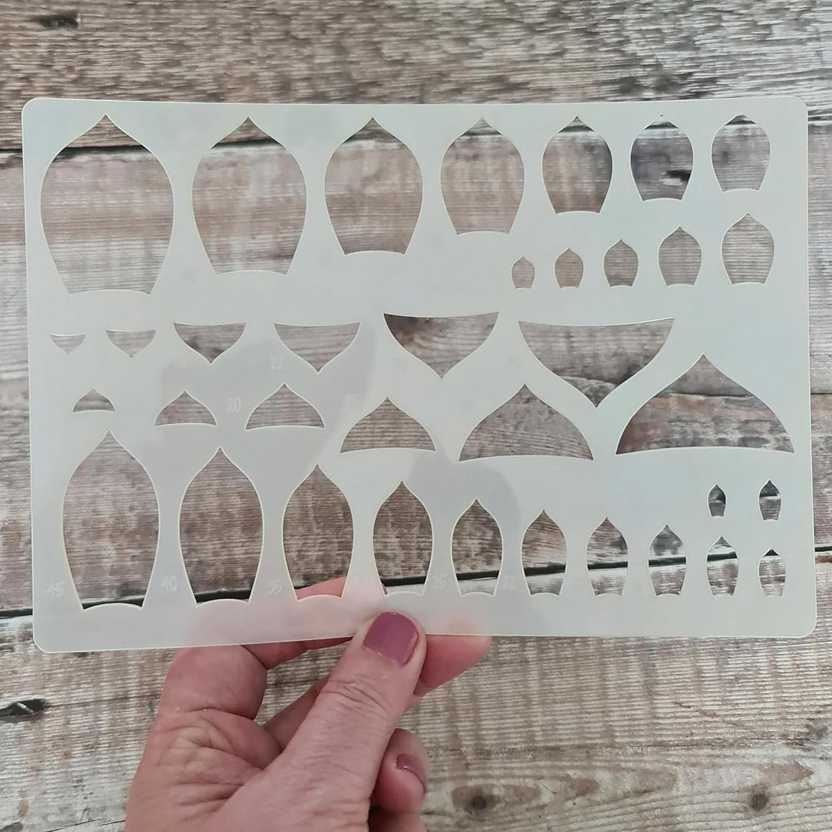 Hand holding a decorative stencil with geometric pattern on a wooden surface