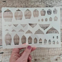 Hand holding a decorative stencil with geometric pattern on a wooden surface