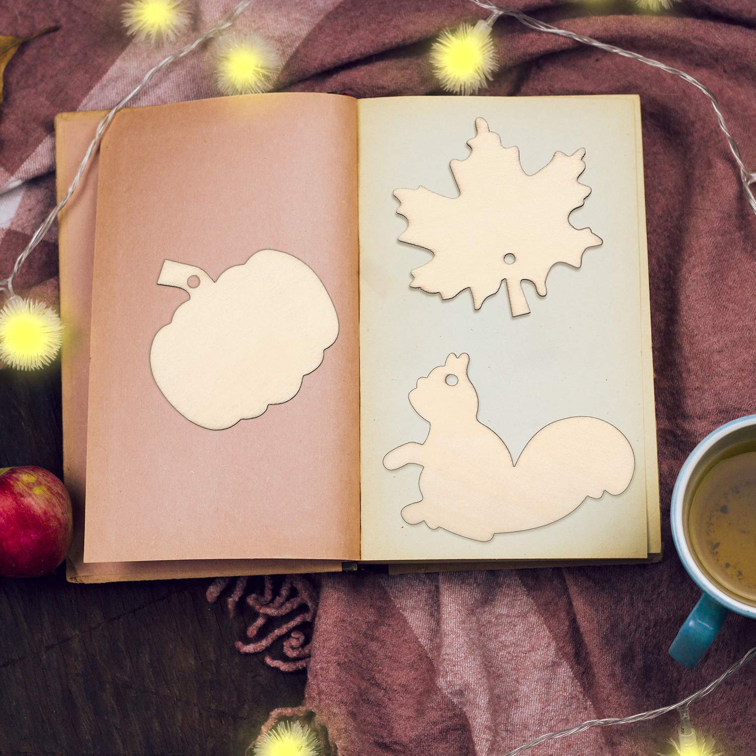 Open book with cut-out shapes of a leaf, pumpkin, and squirrel on a warm-toned fabric background.