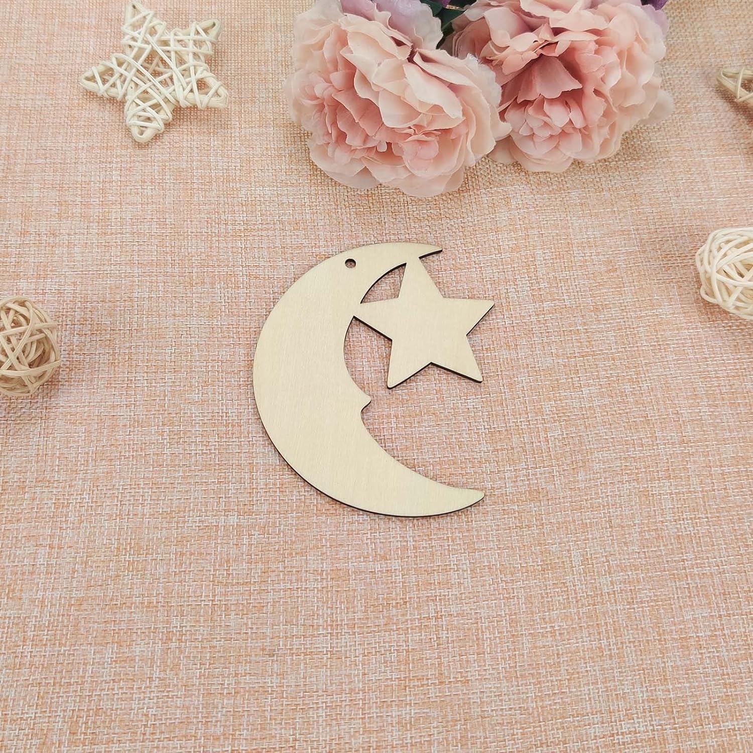 Wooden moon and star ornament on a textured beige surface with flowers and decorative elements.