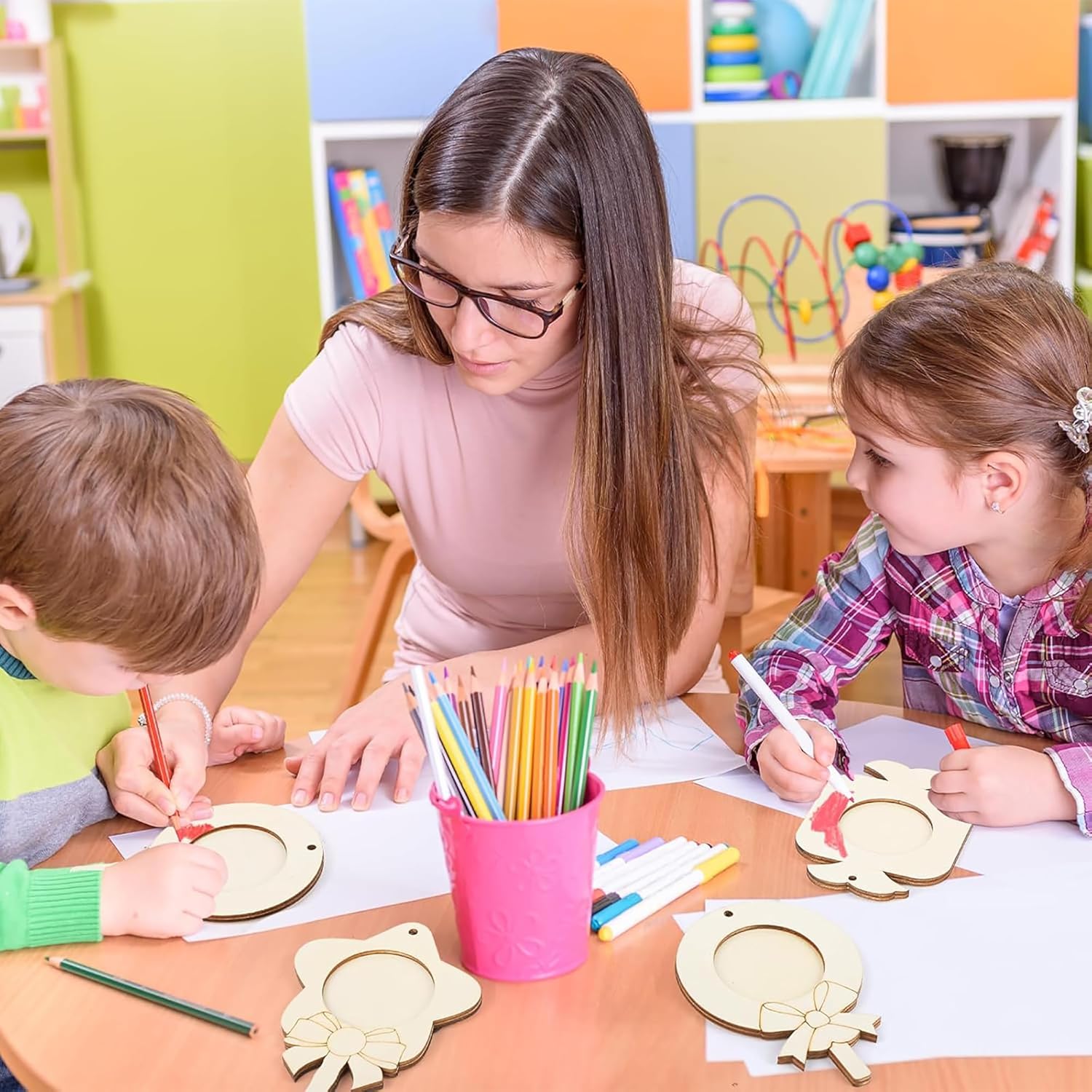 Teacher assisting two children with art projects in a classroom setting