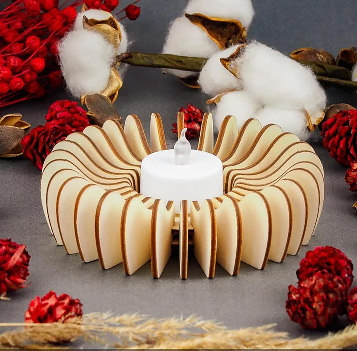Decorative wooden candle holder with a white candle, surrounded by cotton and red flowers on a gray background.