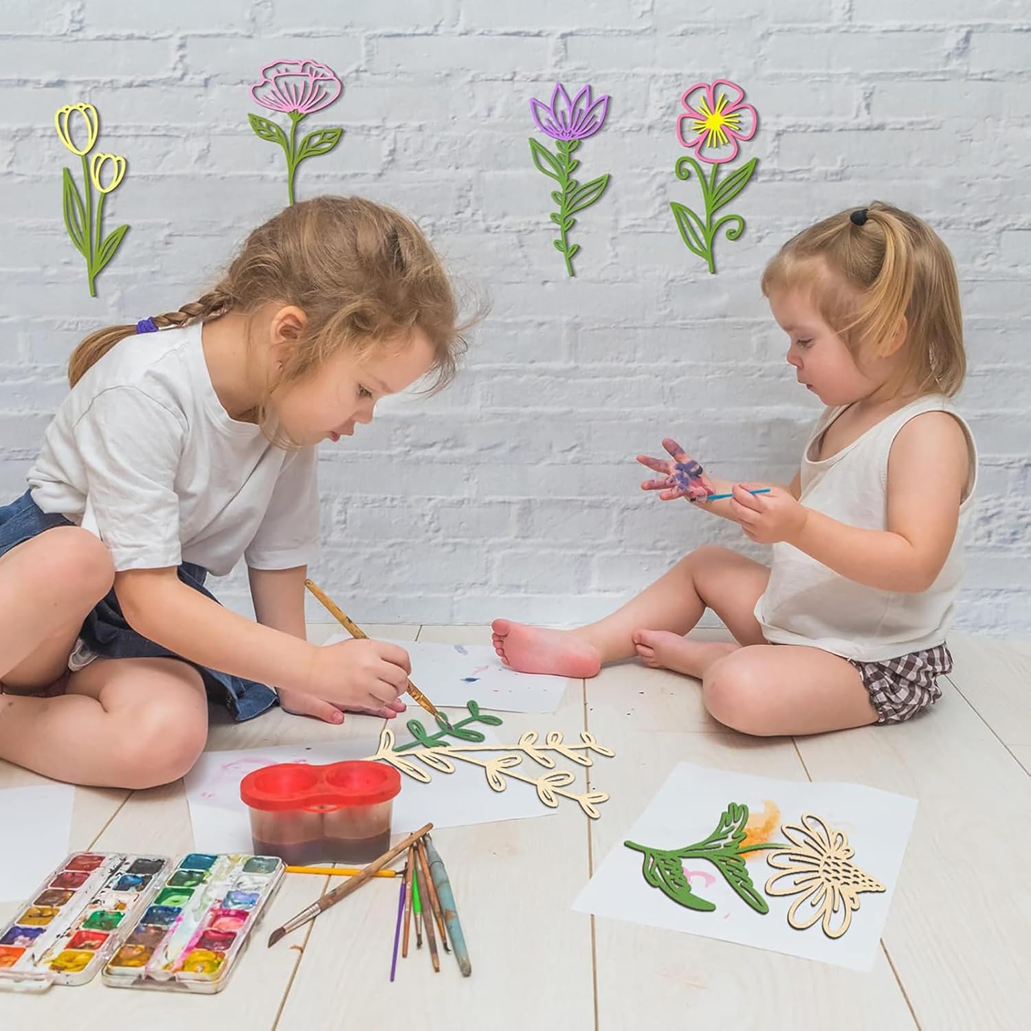 Two children sitting on the floor with art supplies, drawing flowers on paper.