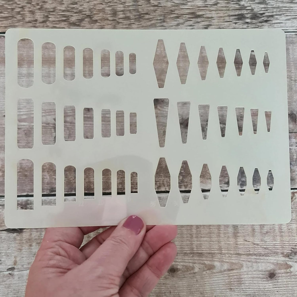 Transparent stenciling template with geometric shapes held by a hand on a wooden surface